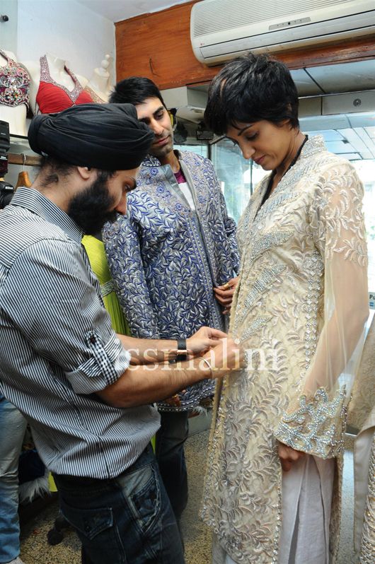 Designer A.D. Singh helps model Jesse Randhawa wear an outfit as husband Sandeep Soparkar looks on