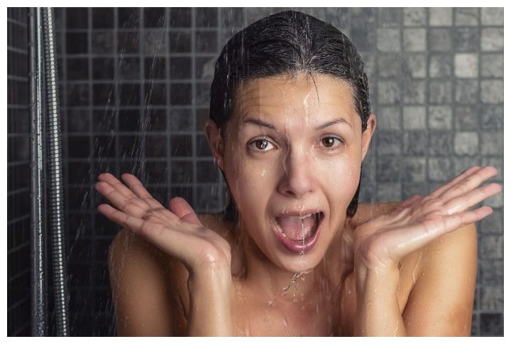Young woman reacting in shock to hot or cold shower water by LarsZ | www.shutterstock.com
