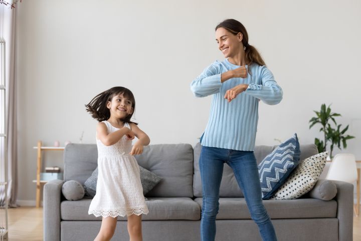 Cheerful mother little daughter standing in living room dancing to favourite song together with her child By fizkes | www.shutterstock.com