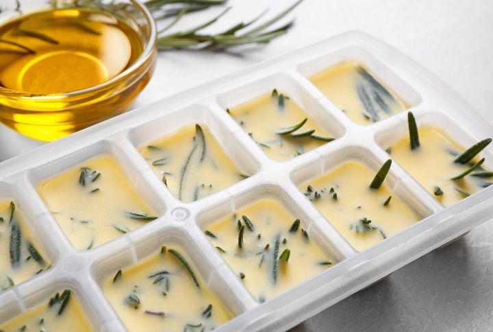 Ice cube tray with herbs frozen in oil and fresh rosemary on grey table, closeup By New Africa | www.shutterstock.com