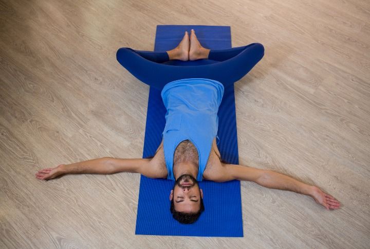 Man doing reclining bound angle pose on exercise mat in fitness studio W By wavebreakmedia | www.shutterstock.com
