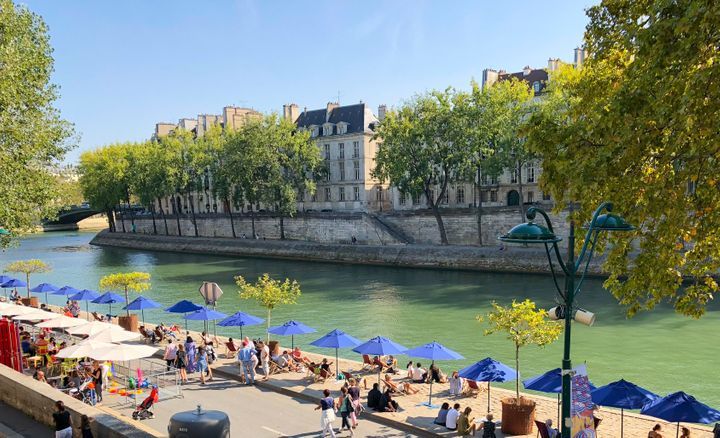 Locals gathered under blue umbrellas. Beach on Seine River in the center of Paris. By Verysmallplanet | www.shutterstock.com