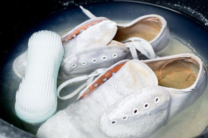 White sneakers in a wash basin soak with washing powder. By Guitar Studio | www.shutterstock.com