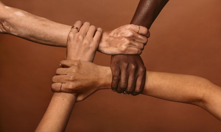 Four diverse women holding each others wrists in a circle. Top view of female hands linked in the lock against brown background by Jacob Lund | www.shutterstock.com